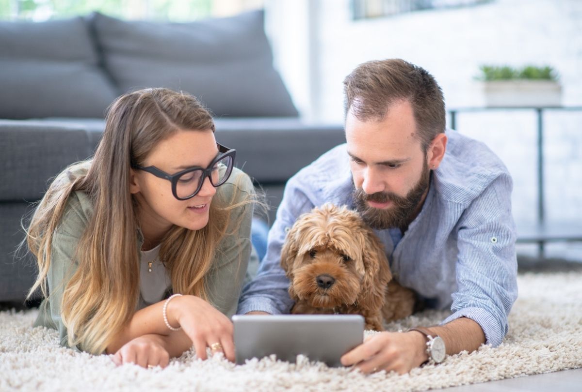 This image of a couple and their dog browsing a tablet in their home represents financial decisions couples make together for their financial future.