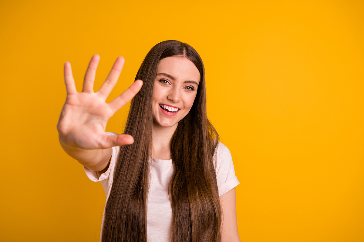 This image of a young woman holding up five fingers represents the five steps outlined in InvestRight's blog on retirement planning that you can take to kickstart your retirement savings.