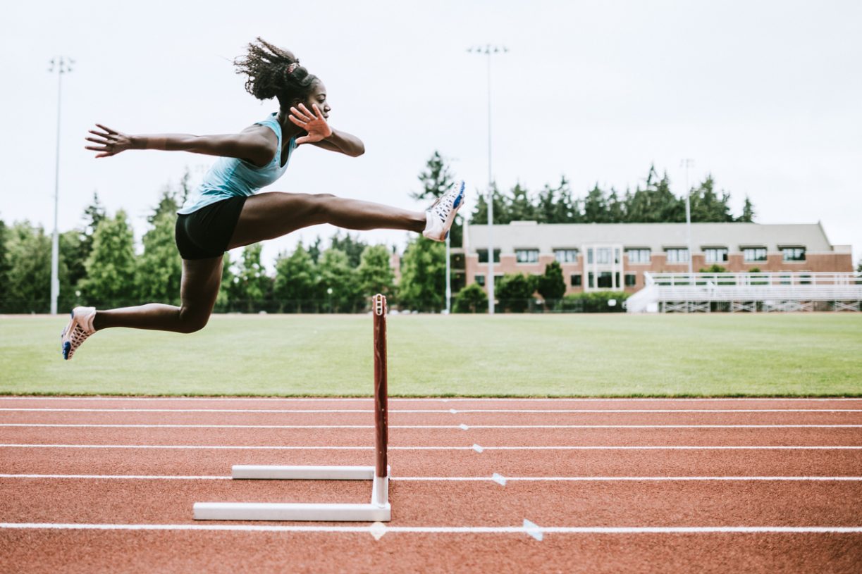 This image of an athlete jumping over a hurdle on an outdoor track represents common investing barriers that can act as obstacles on our investor journeys, but there are ways to overcome them and continue on the road to becoming a confident and informed investor.