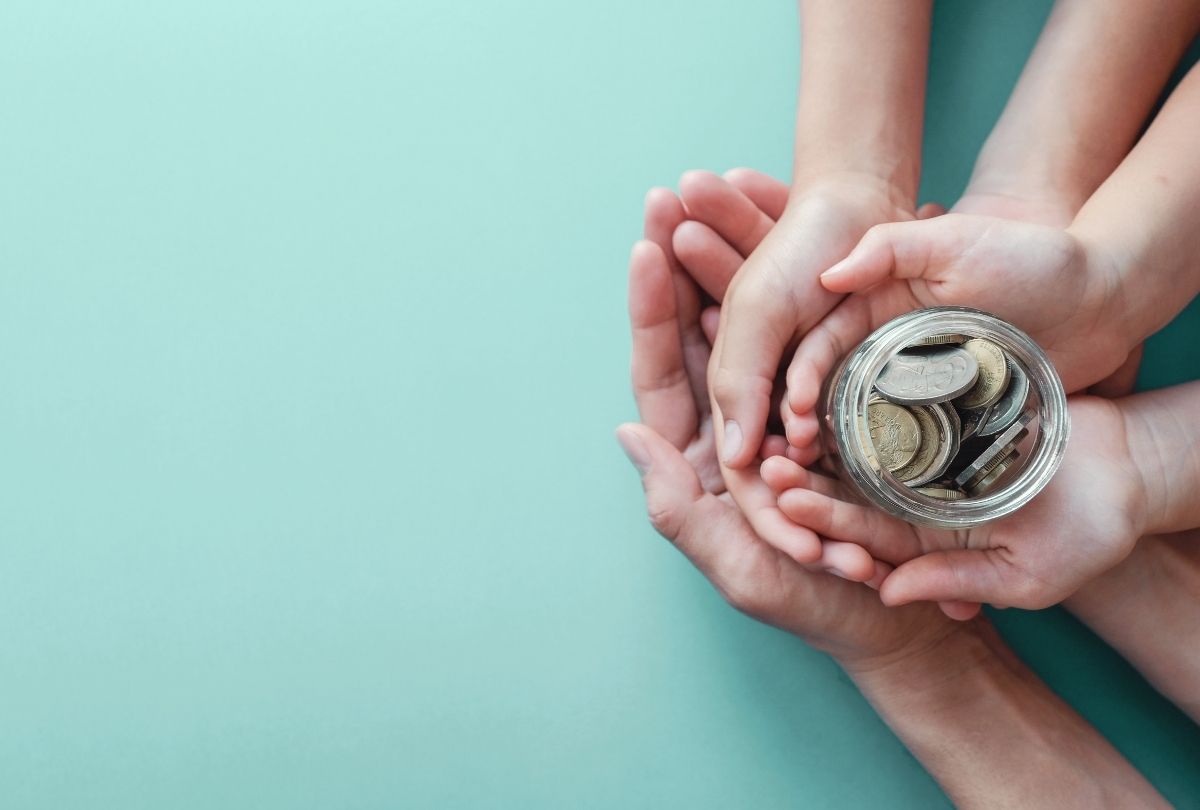 This image of two parents and their young child embracing each other and holding a jar of coins represents the idea of starting to save early when building a child's education fund.